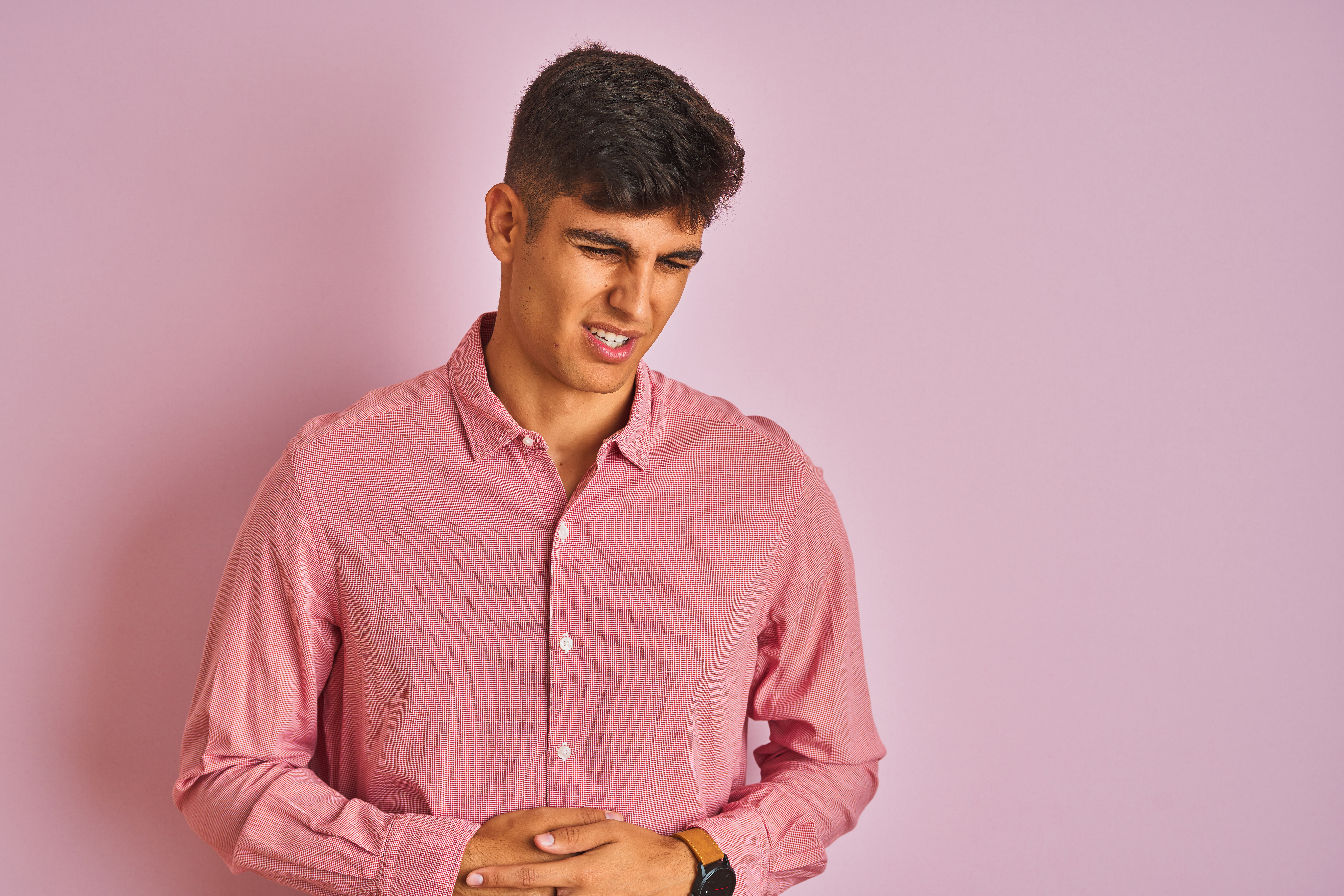 Young indian man wearing elegant shirt standing over isolated pink background with hand on stomach because indigestion, painful illness feeling unwell. Ache concept.