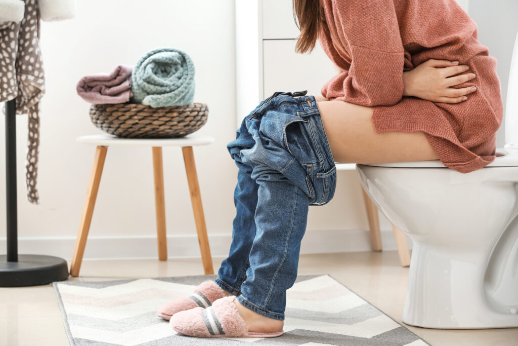 Young woman sitting on toilet bowl in restroom
